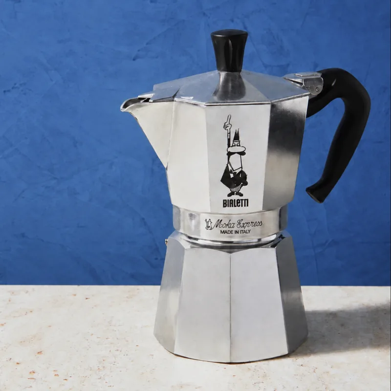 Bialetti Moka Express with a black handle against a blue wall